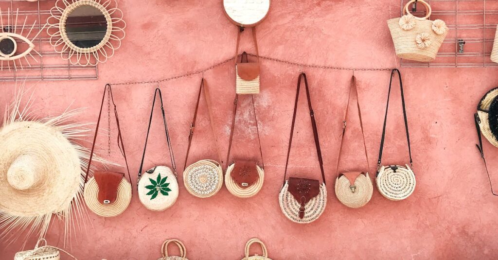 Aesthetic display of handmade wicker and straw accessories against a textured pink wall.